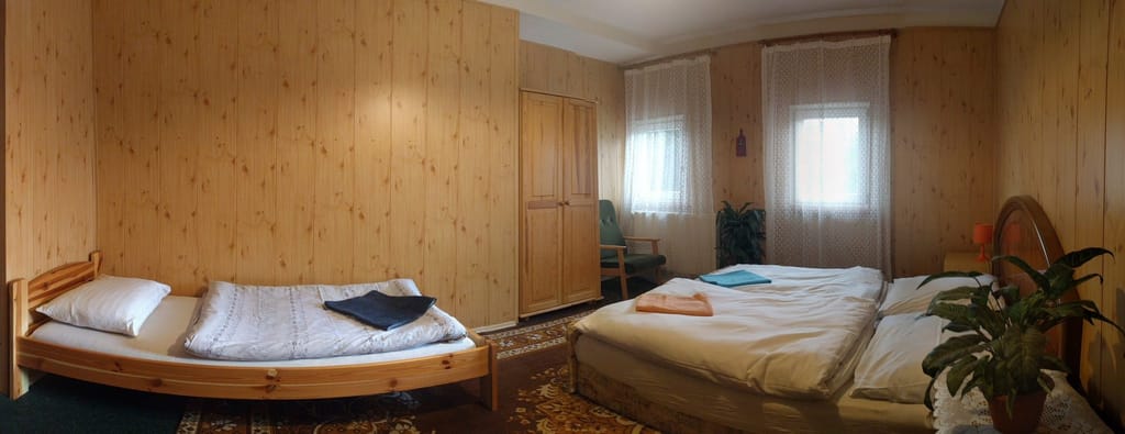 Pokoj obložený světlým dřevem se třemi lůžky a pokojovou rostlinou